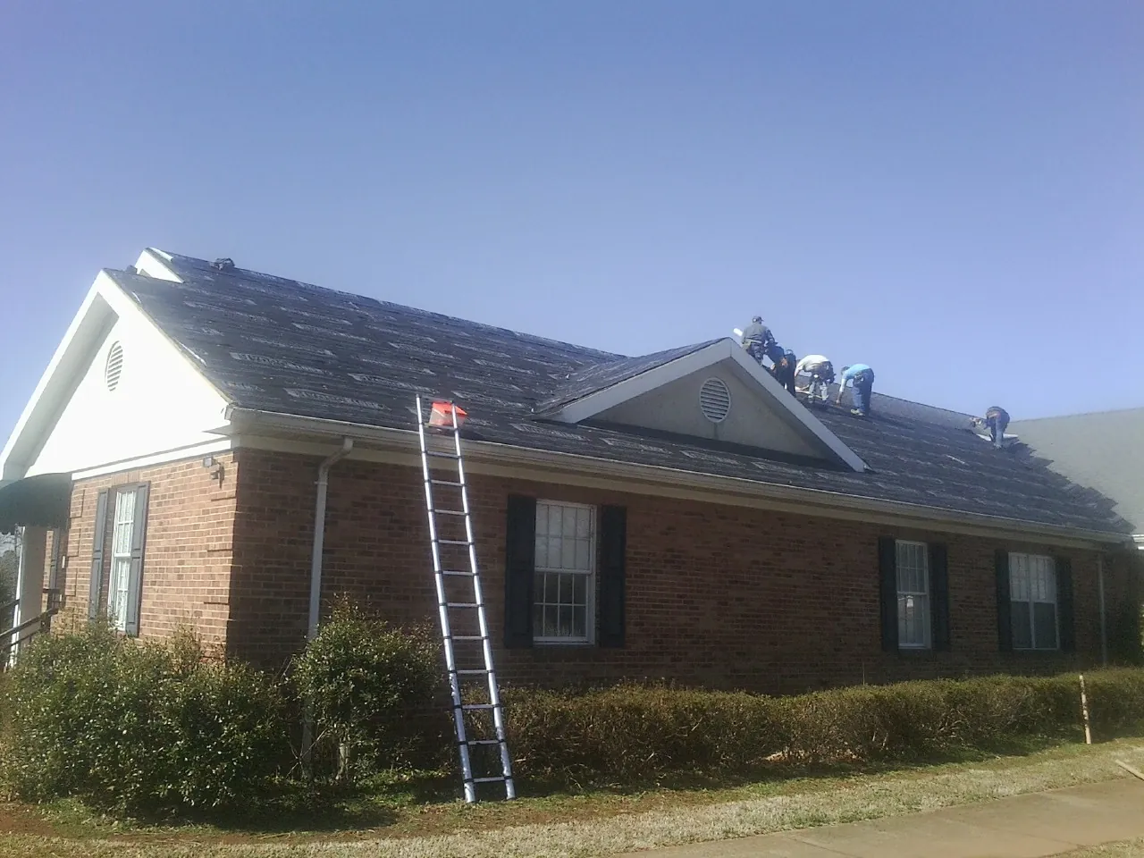 Crew tearing shingles off a brick ranch roof with a ladder set — Metal Roof Repair work by our crew in Scottsboro