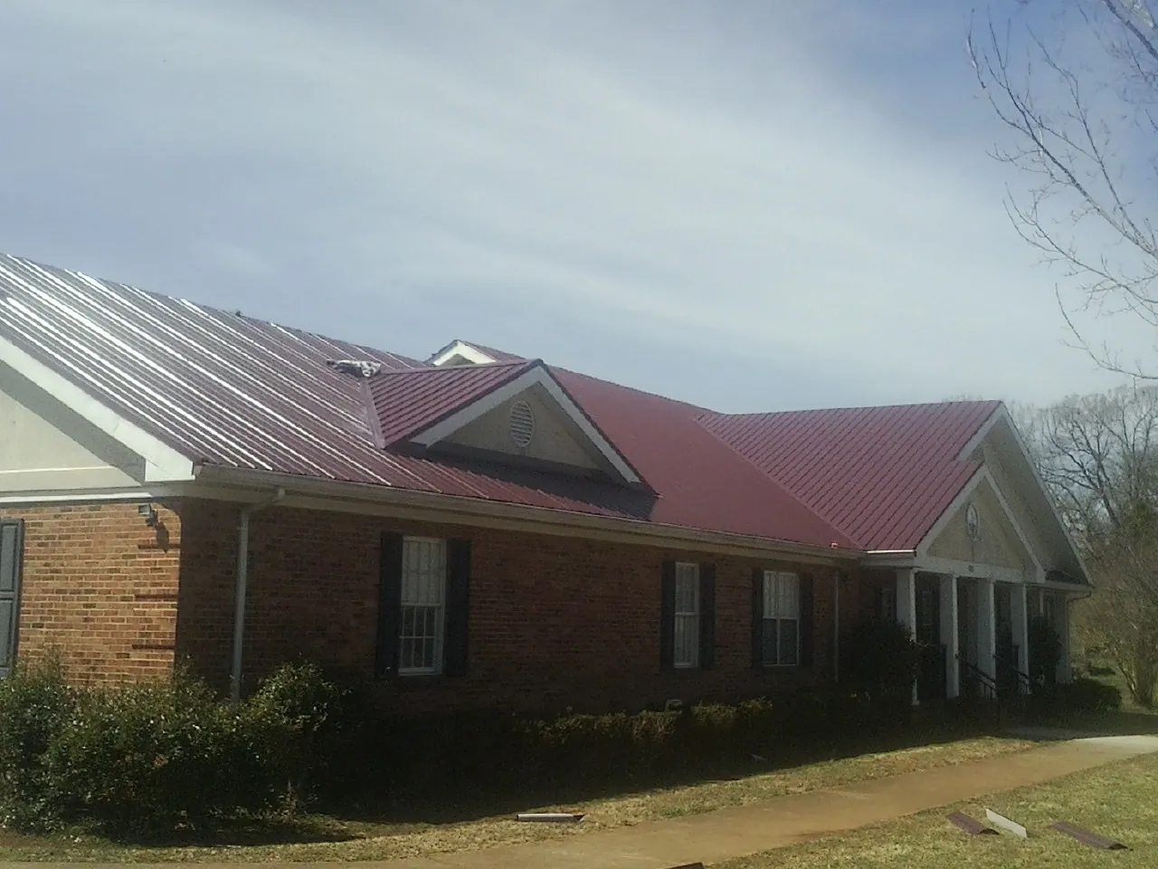 Red metal roof with gabled entries on a long brick building, from a Hail Damage Roof Repair job in Scottsboro