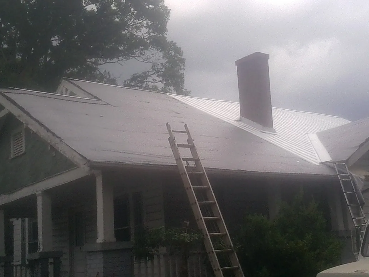 Ladders against a metal roof on an older home with a brick chimney in Scottsboro