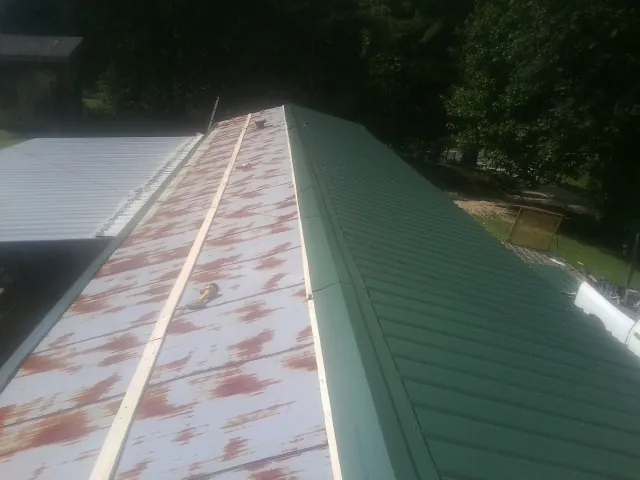Old rusted panels beside newly installed green metal roofing — Wind Damage Roof Repair by Roofing Brothers in Scottsboro