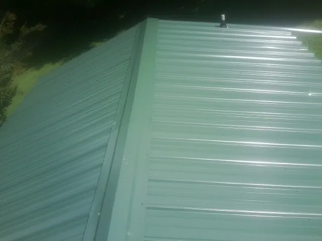 New green metal panels meeting at the ridge of a roof — Flat Roof Repair work by our crew in Scottsboro