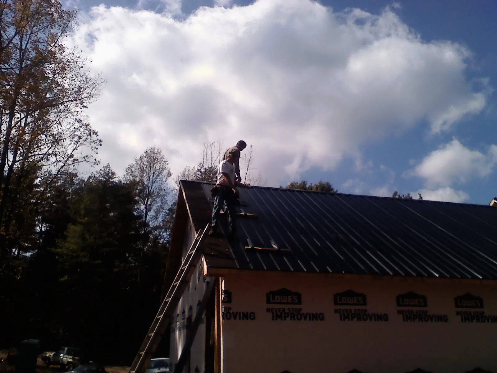 Roofer fastening dark metal panels high against a cloudy sky, from a Roof Inspection job in Scottsboro