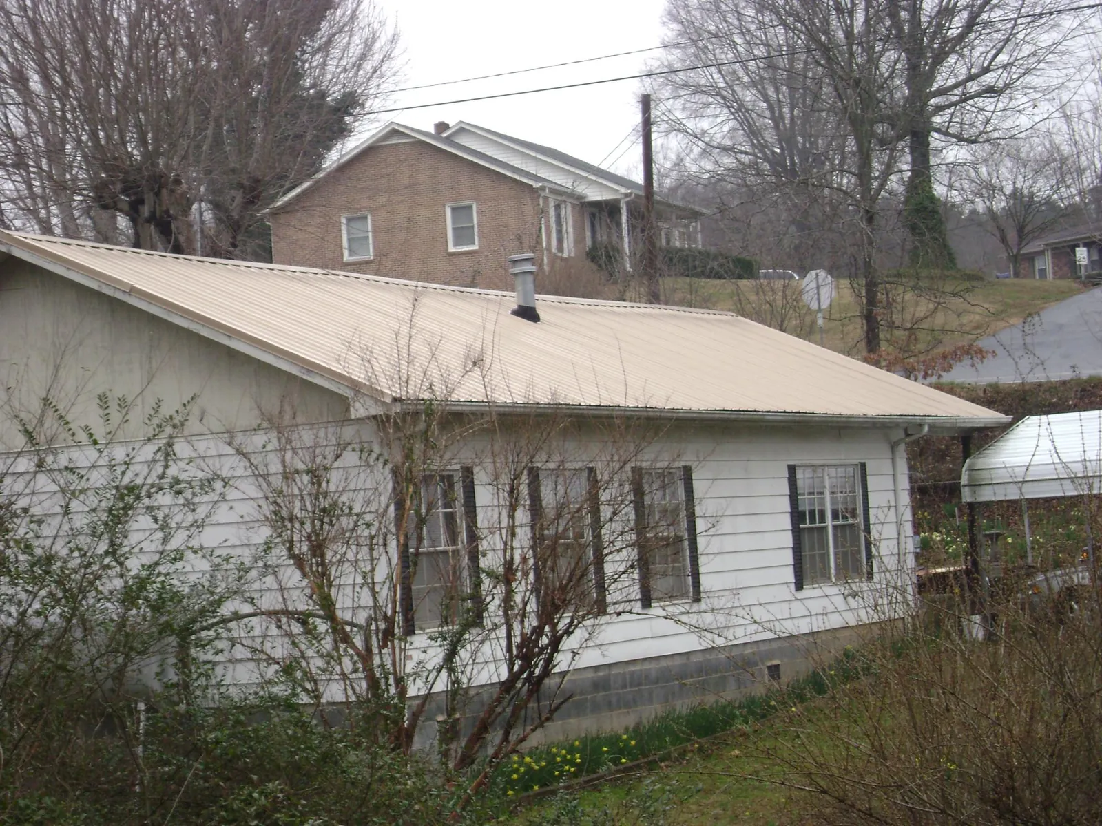 Tan metal roof on a white sided house set into a hillside — Commercial Roofing by Roofing Brothers in Scottsboro